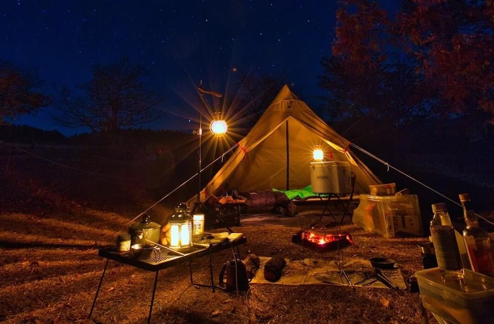 A campsite at night with a lit tent and lanterns