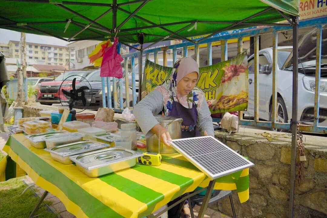 A food vendor at a covered market stall with a solar panel on the table