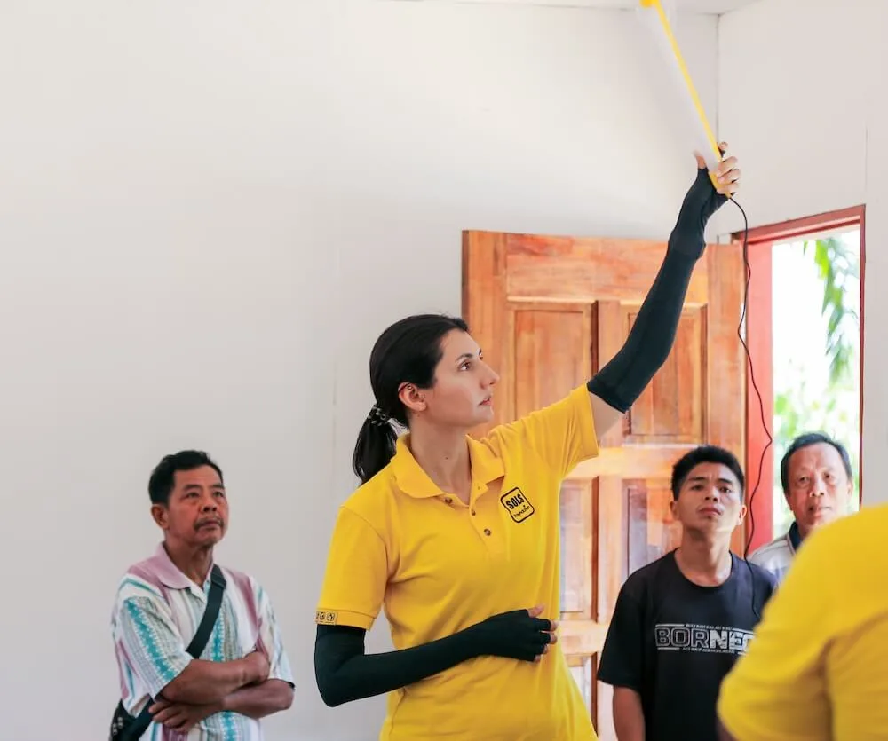 A SOLS Life team member fitting a ceiling light while villagers watch