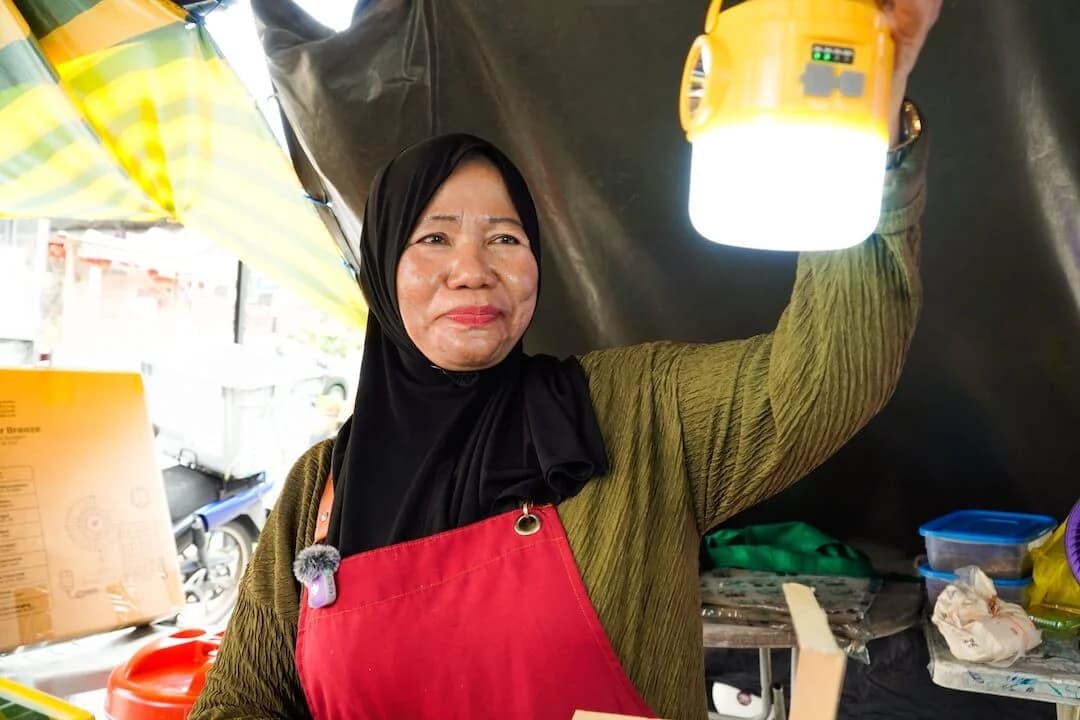 A market vendor holding up a lit solar lamp at her stall