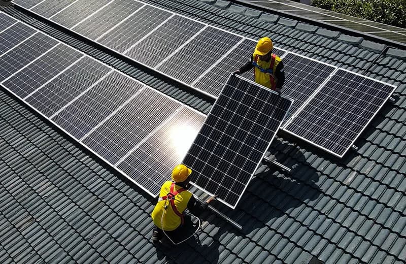 An installer kneeling among solar panels on a tiled roof