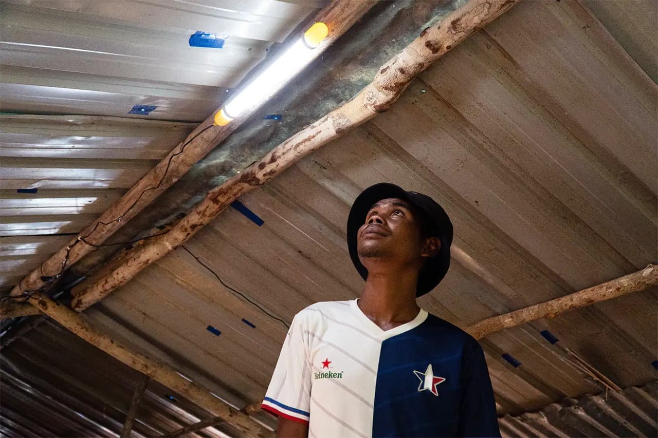 A man looking up at a lit solar tube light fixed to the roof beam of his home