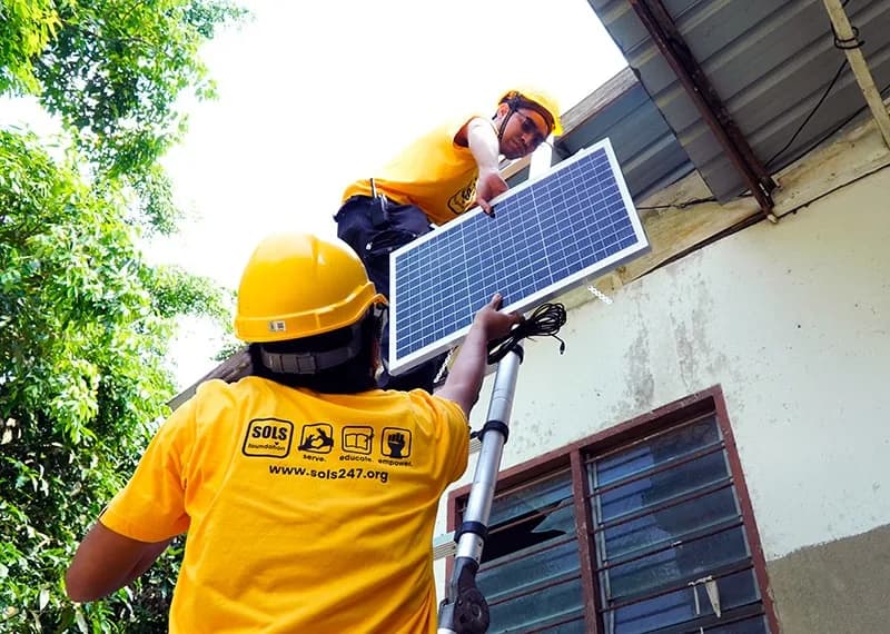 Two technicians in SOLS shirts and hard hats mounting a solar panel on a wall